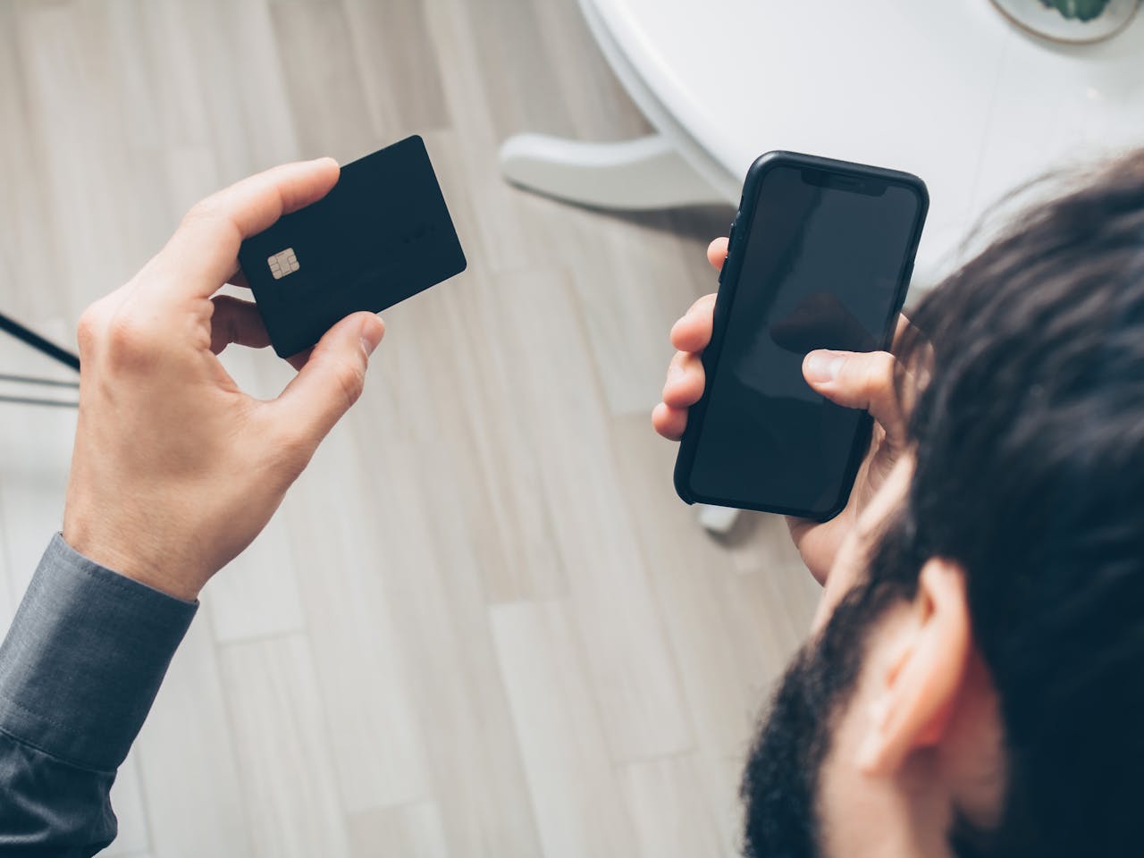 Close-up of man holding a smartphone and credit card, making an online payment indoors.